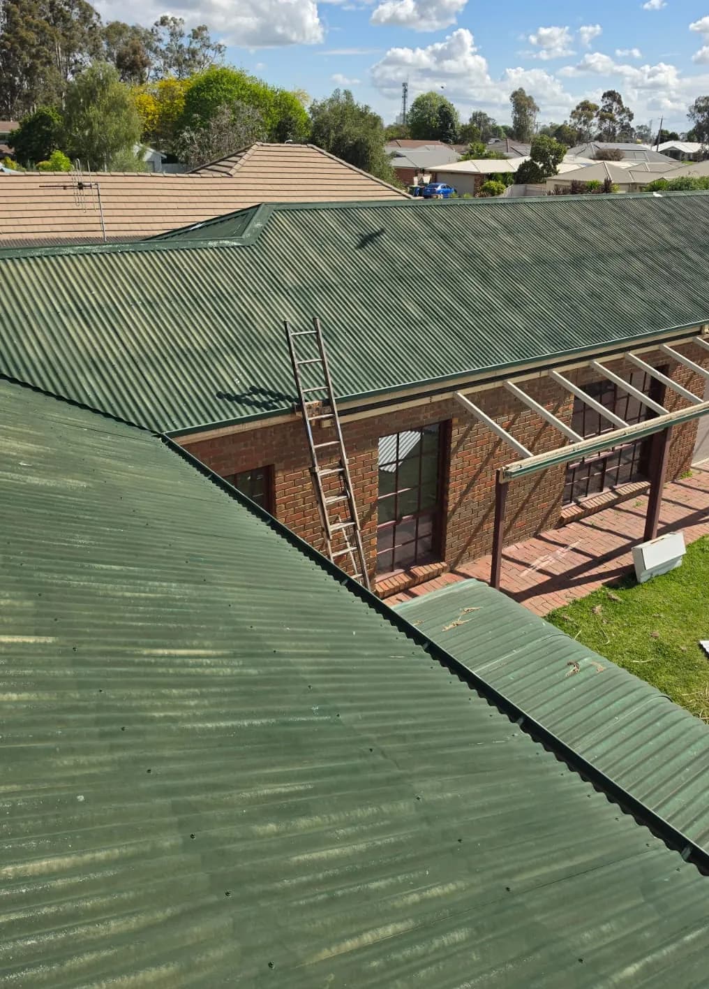 Brick home in Numurkah with a streaky, chalky green corrugated roof and a ladder against the gutter, before